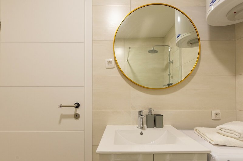 Badezimmer mit Spiegel, Waschbecken und Schränken.