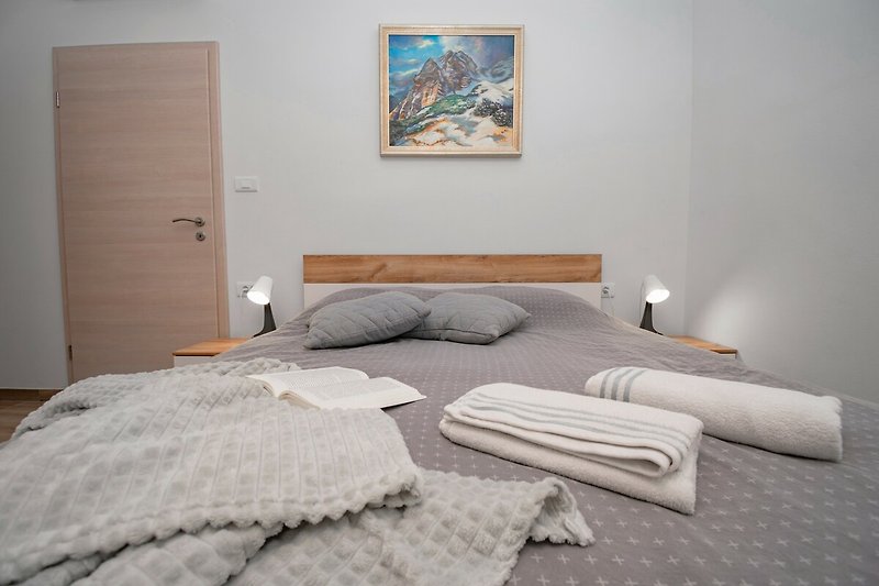 Gemütliches Schlafzimmer mit Holzbett, Kunst an der Wand und gemusterten Bettwäsche.