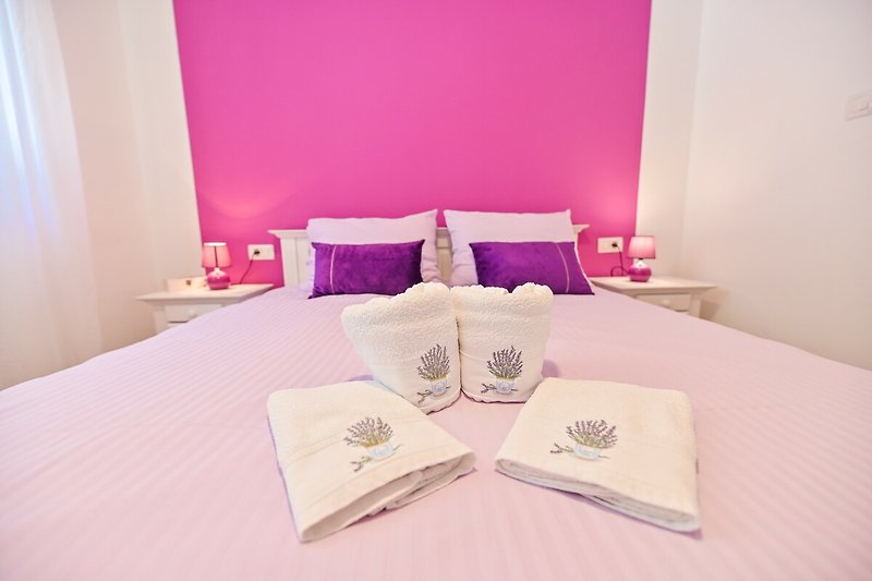 Lila Schlafzimmer mit gemütlichem Bett und violetten Kissen.
