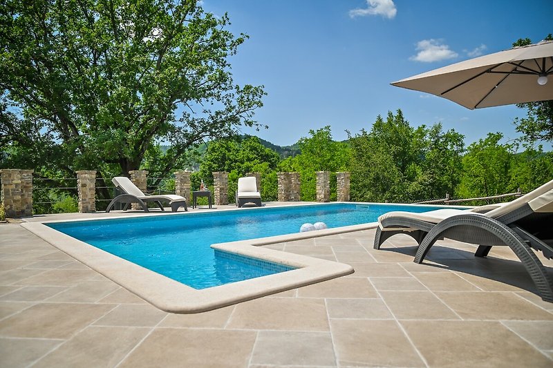 Luxuriöser Poolbereich mit Sonnenliegen, Schirmen und Pflanzen.