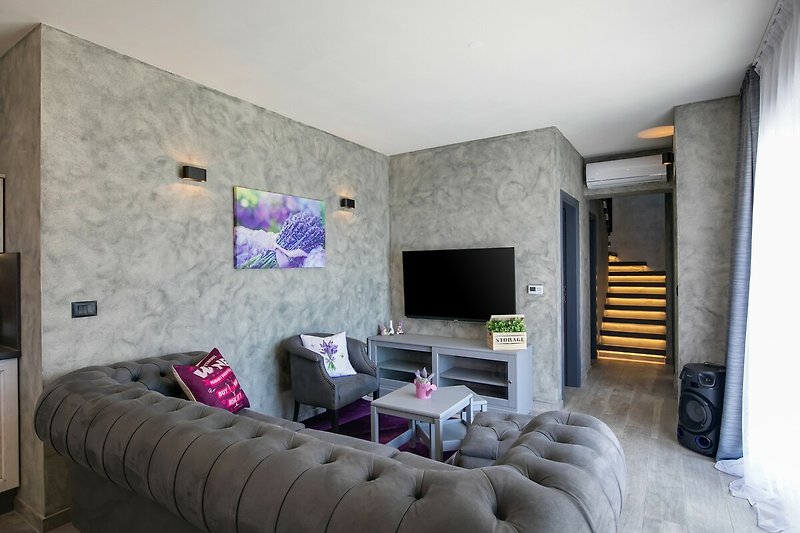 Gemütliches Wohnzimmer mit lila Couch, Holzboden und modernem Design. Entspannen Sie sich in stilvollem Ambiente.