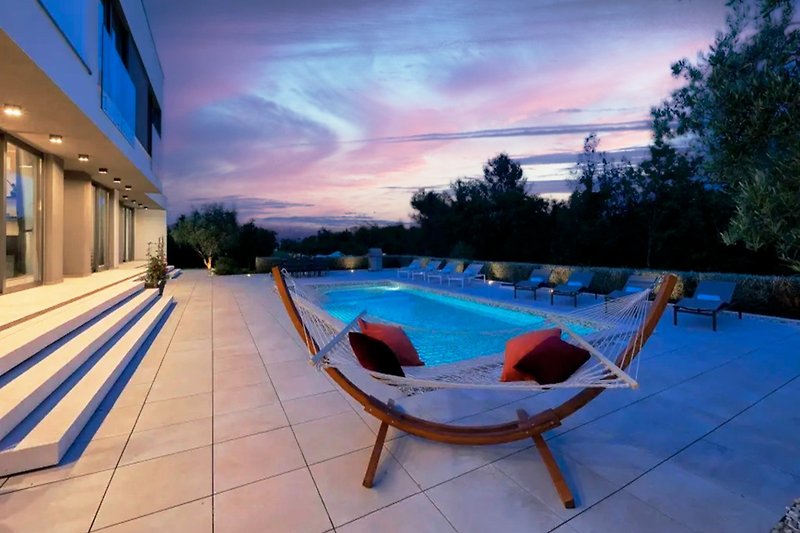 Luxuriöser Pool mit Sonnenliegen und Abendstimmung.