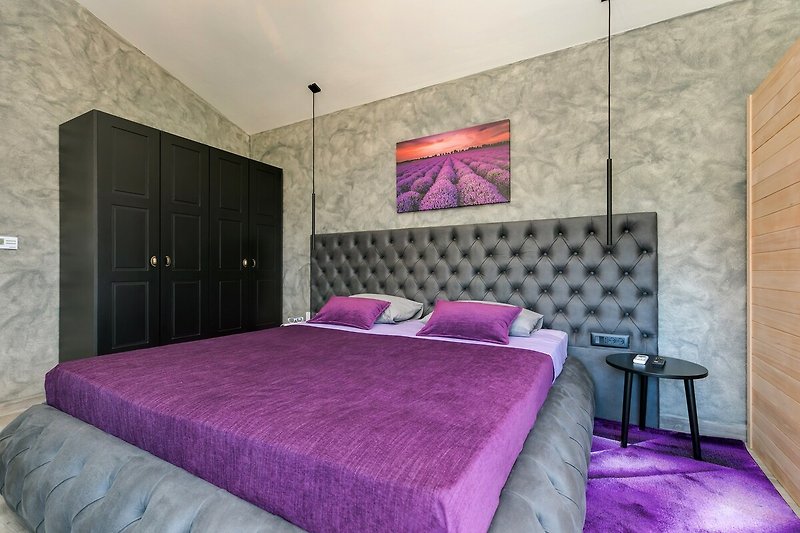 Gemütliches Schlafzimmer mit lila Bettwäsche und Holzmöbeln. Entspannen Sie sich in stilvollem Ambiente.