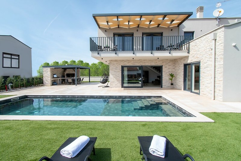 Modernes Haus mit Pool, Fenstern, Pflanzen und blauem Himmel. Ideal für Entspannung!