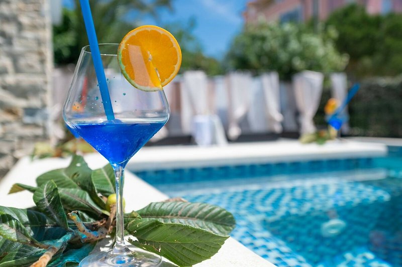 Erfrischender Pool mit Blick auf tropische Landschaft und Glas mit Getränken.