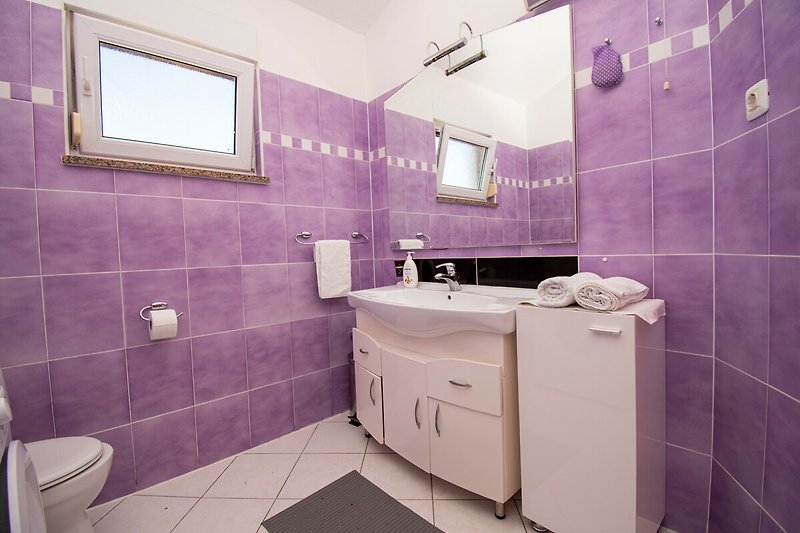 Badezimmer mit lila Waschbecken, Armatur und Badezimmerschrank.