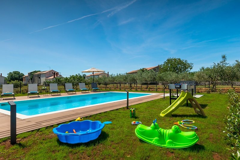 Schwimmbad mit Außenmöbeln und grüner Landschaft.