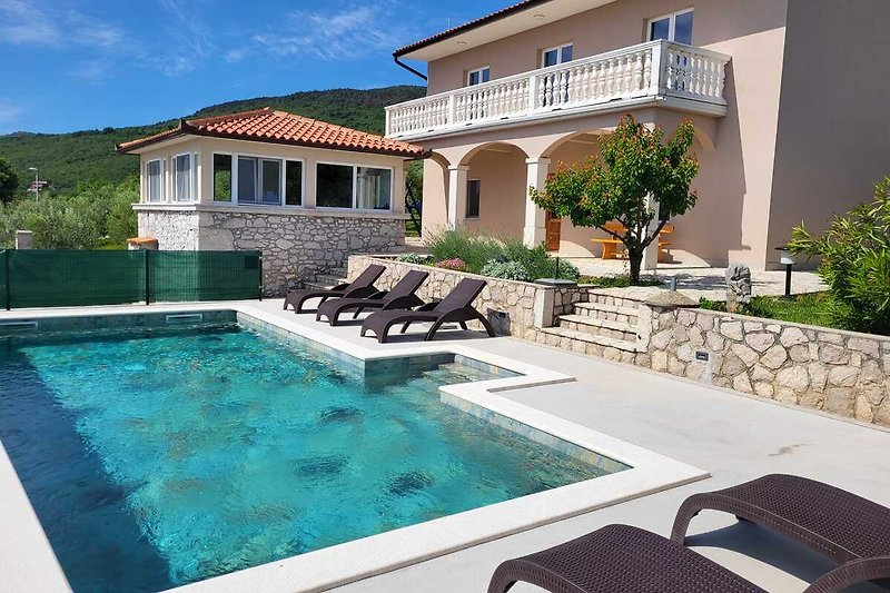 Villa mit Pool, Liegestühlen, Pflanzen und Blick auf den blauen Himmel.