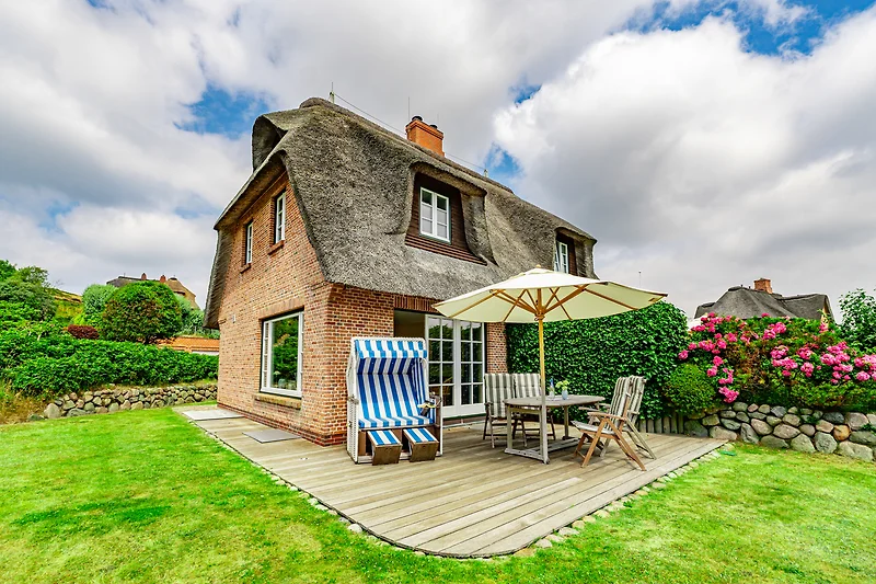 Reetgedecktes Bauernhaus an der Küste mit gepflegtem Garten.
