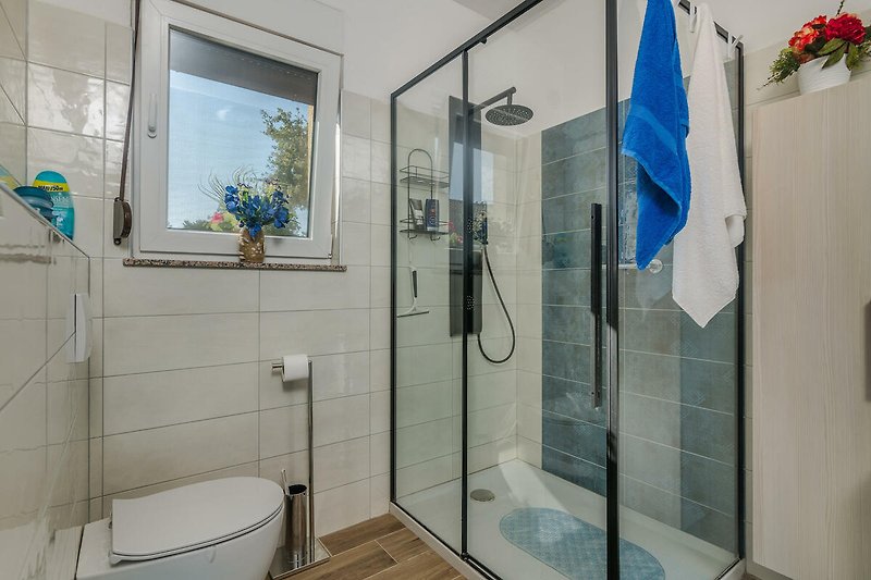 Modernes Badezimmer mit blauer Dusche, Spiegel und Fenster.