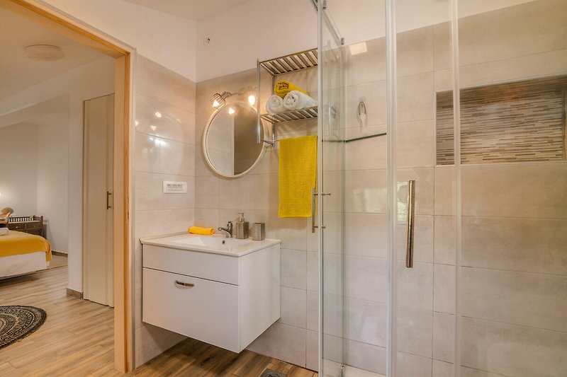 Badezimmer mit Spiegel, Waschbecken, Duschkopf und Holzmöbeln.
