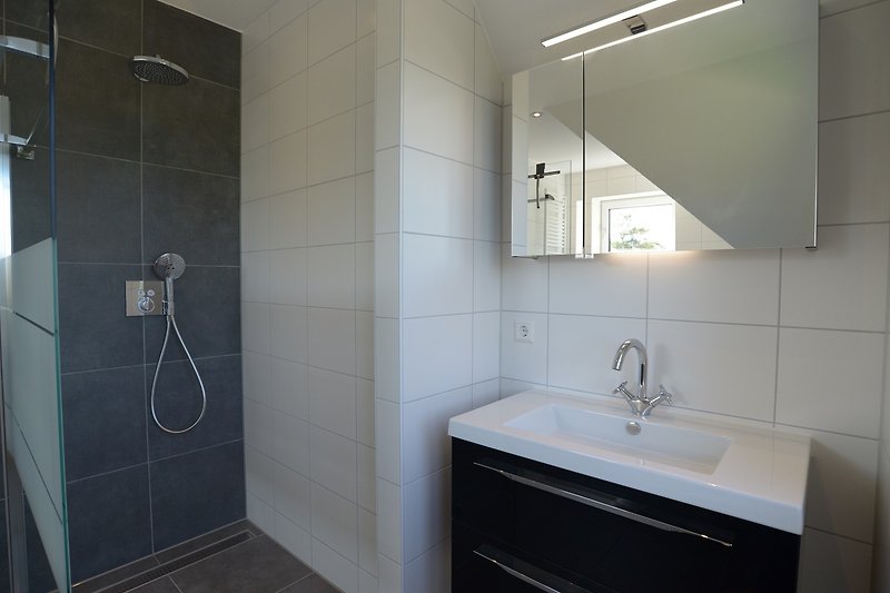 Modernes Badezimmer mit Spiegel, Waschbecken, Dusche und Fliesen.
