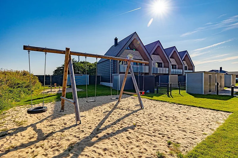 Speeltoestel met glijbanen en klimmuren in een park, omringd door groen gras en enkele bomen. Kinderen kunnen klimmen, glijden en spelen in een veilige en uitnodigende omgeving.
