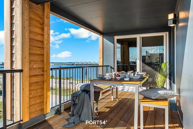 Terrazza con vista sul mare, arredata con un tavolo e sedie in ferro battuto, circondata da piante e fiori colorati.