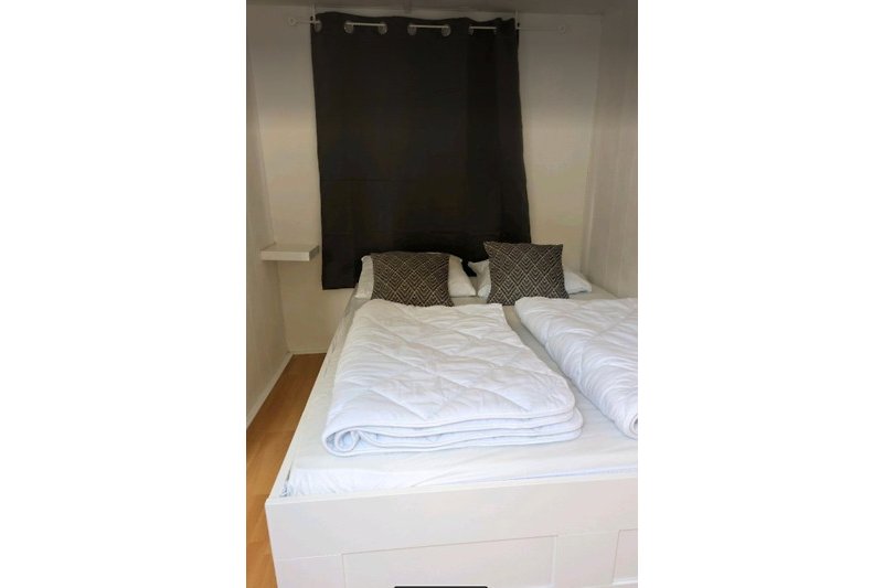 Schlafzimmer mit Holzmöbeln, Bett, Kissen, Lampe, Wand und Decke.