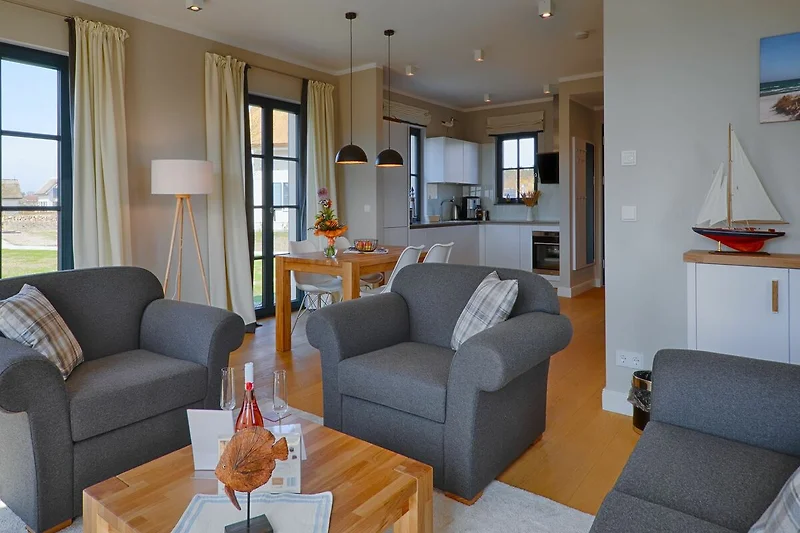 Soggiorno con divano grigio, tavolino in legno e tappeto beige. Le pareti sono decorate con quadri moderni e c'è una grande finestra con tende bianche che forniscono molta luce naturale.
