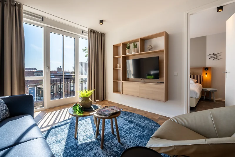Helles Wohnzimmer mit Sofa, Sessel, Tagesbett und Zugang zum Balkon.