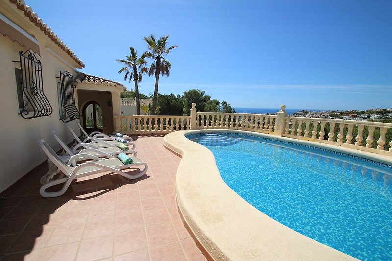 Luxuriöser Pool mit Palmen und Sonnenliegen am Meer.