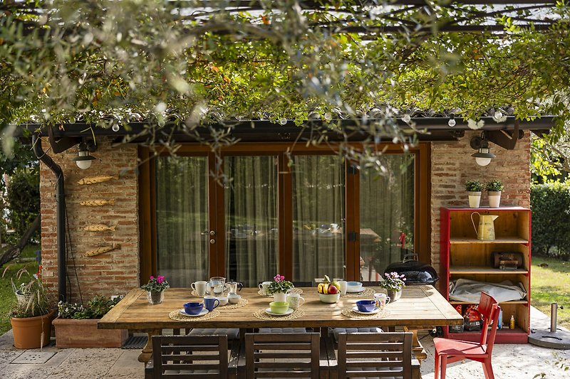 Un'immagine di un patio con mobili da esterno, tavolo, sedie e piante.