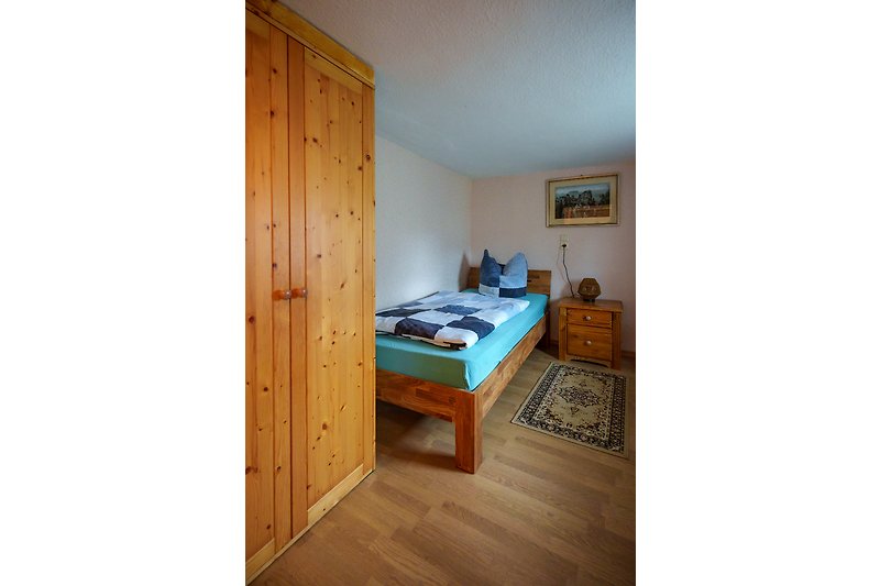 Einzelzimmer mit Holzmöbeln und bequemem Bett.