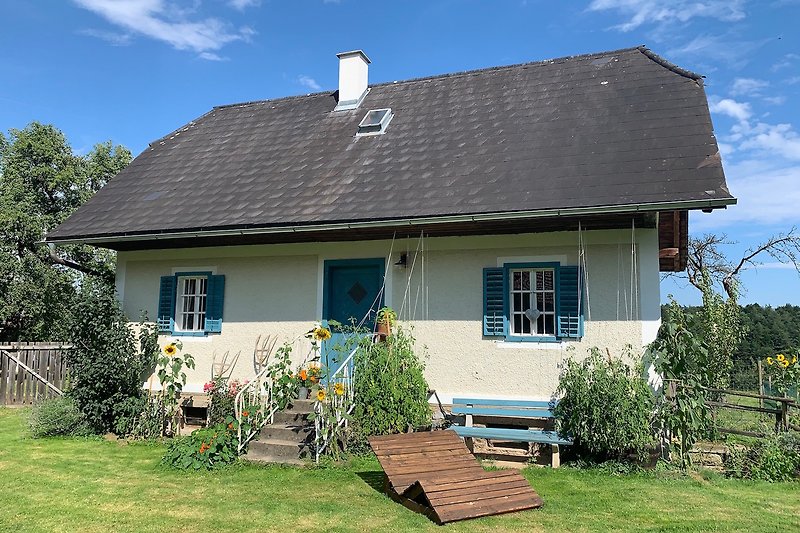 Charmantes Landhaus mit Garten, Bäumen und gemütlicher Sitzbank.