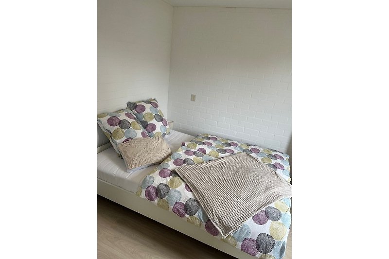 Gemütliches Schlafzimmer mit lila Bettwäsche und Holzbettgestell.