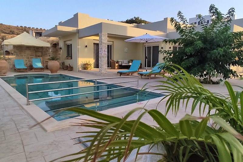 Stunning view of a modern property with a swimming pool, surrounded by lush greenery and outdoor furniture.