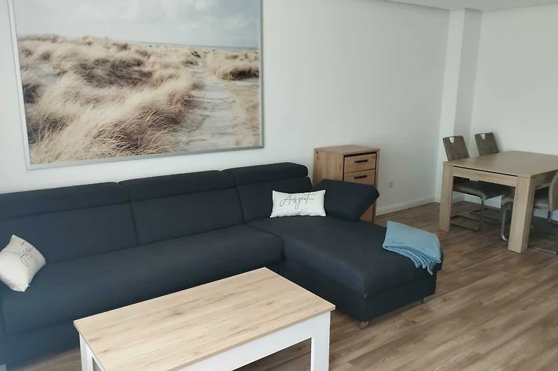 Wohnbereich mit Sofa, Sessel, Couchtisch und dekorativer Zimmerpflanze.