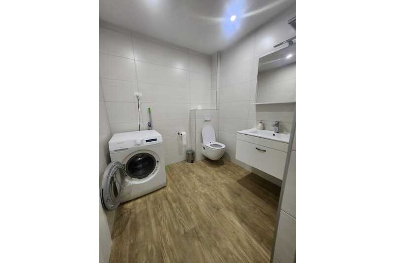 Moderne Badzimmer mit Waschmaschine, Dusche und Waschbecken.