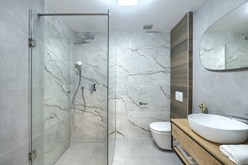Modernes Badezimmer mit Glasdusche, Spiegel und Armatur.