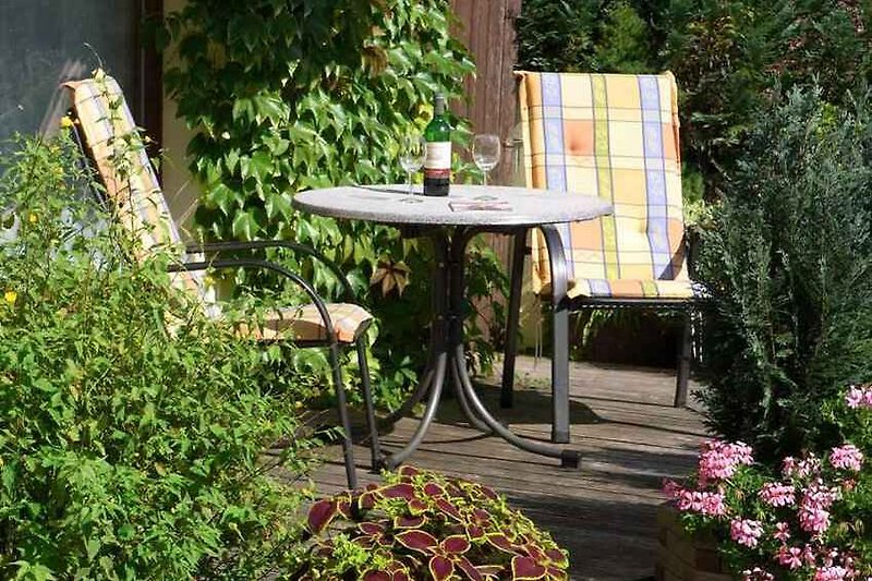 Terrasse mit Pflanzen, Tisch und Stühlen.