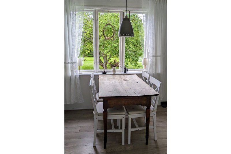 Holzstühle und Tisch vor Fenster mit Vorhang und Lampe.