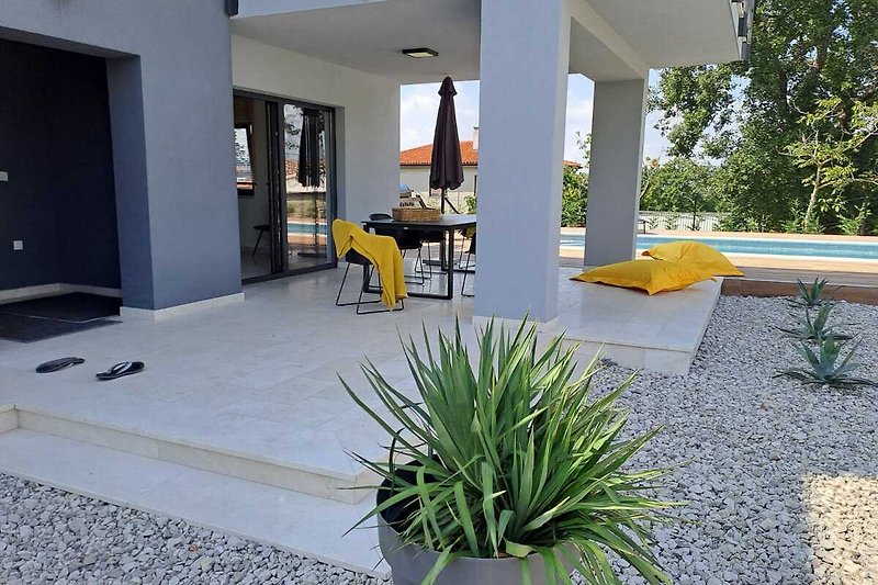 Eine idyllische Terrasse mit Tisch und Stühlen, umgeben von Pflanzen und einem schönen Gebäude.