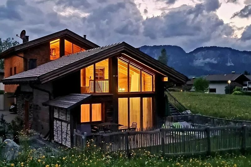 Abendstimmung: Holzhaus mit Bergblick und blühendem Garten.