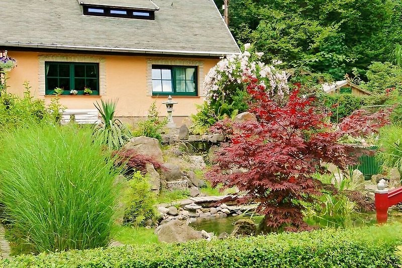 Gemütlicher Garten mit Blumen, Bäumen und einem charmanten Haus.