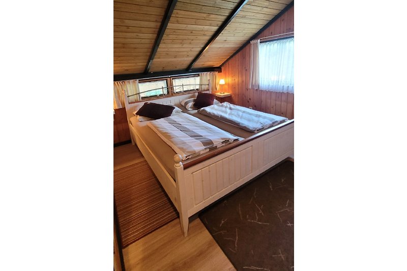 Gemütliches Schlafzimmer mit Holzbett, Lampe und gemütlicher Bettwäsche.