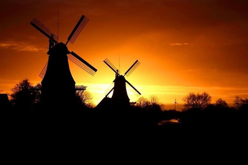 Windmühle in der Abenddämmerung mit rotem Himmel am Horizont.