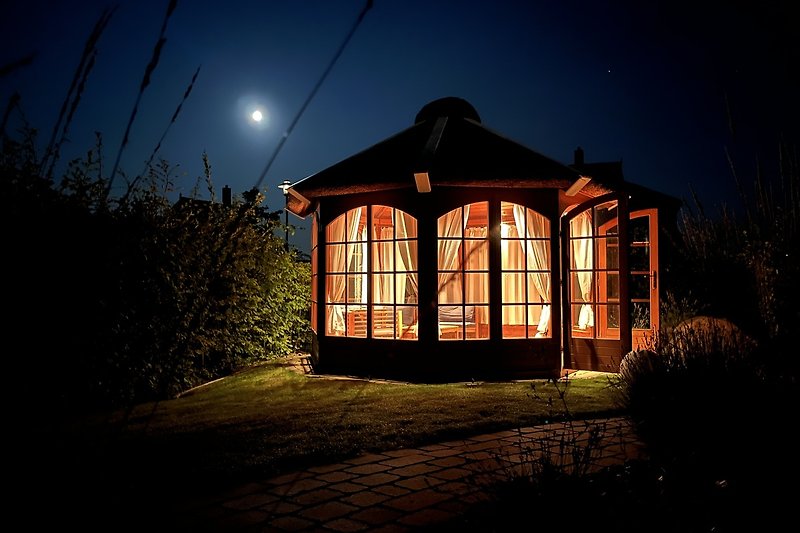 Schönes Haus mit winterlichem Nachthimmel und beleuchtetem Garten.