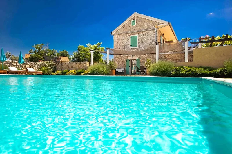 Großer Pool mit Sonnenliegen und Blick auf gepflegte Gartenanlage.