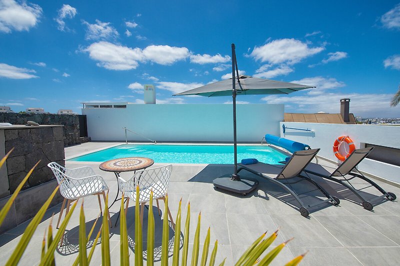 Elegante Sonnenliegen am Pool mit Blick auf das Meer und Palmen.