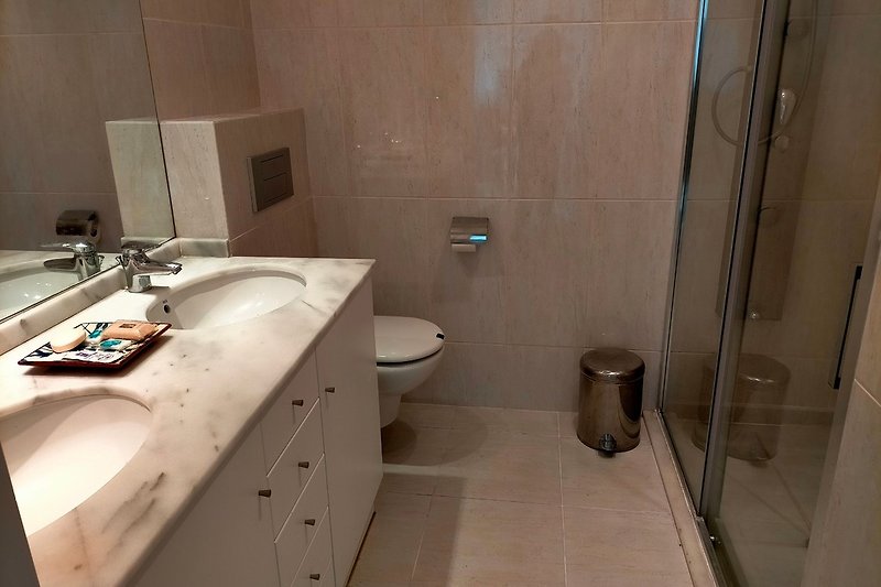 Cremefarbenes Marmorbad mit Doppelwaschbecken und großer ebenerdiger Dusche.