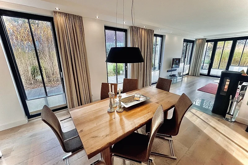 Wohnzimmer mit Holz-Esstisch, Couch, Pflanzen und stilvollem Lampendesign.