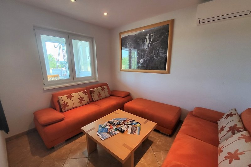 Wohnzimmer mit gemütlicher Couch, Tisch, Holz, Satellitenfernsehen und Dekoration.