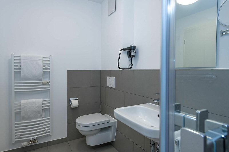 Badezimmer mit Dusche, Waschtisch, WC, Spiegel und Handtuchwärmer