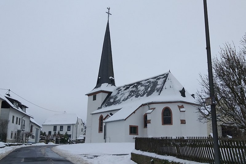 Historisches Gebäude mit Kirche, Kapelle und Turm in einem winterlichen Dorf.