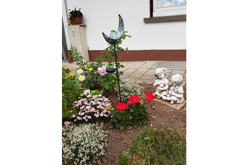 Gemütliches Ferienhaus mit blühenden Pflanzen, Vogel und Kunstwerk.
