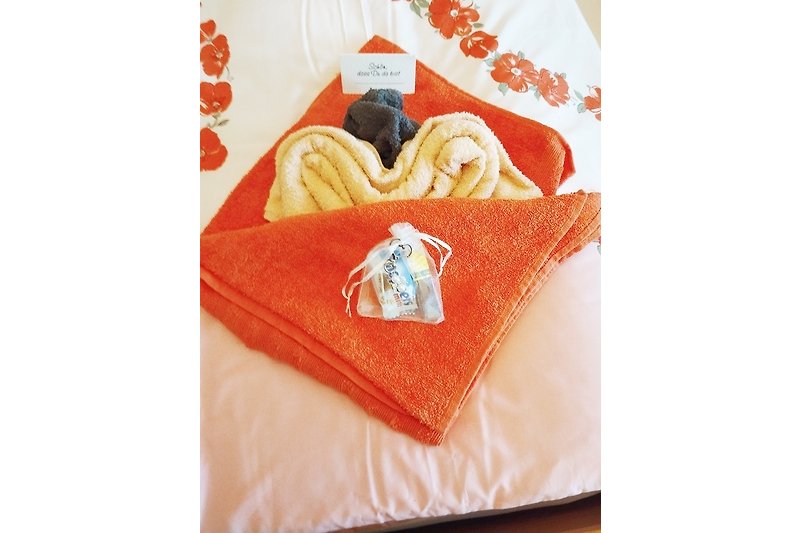 Gemütliches Ferienhaus mit orangefarbenem Kissen, rechteckigem Tisch und frischen Bettwäsche.