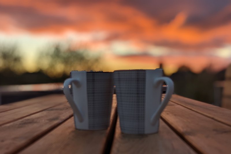 Holzterrasse mit Meerblick, Sonnenuntergang und Kaffeetasse.