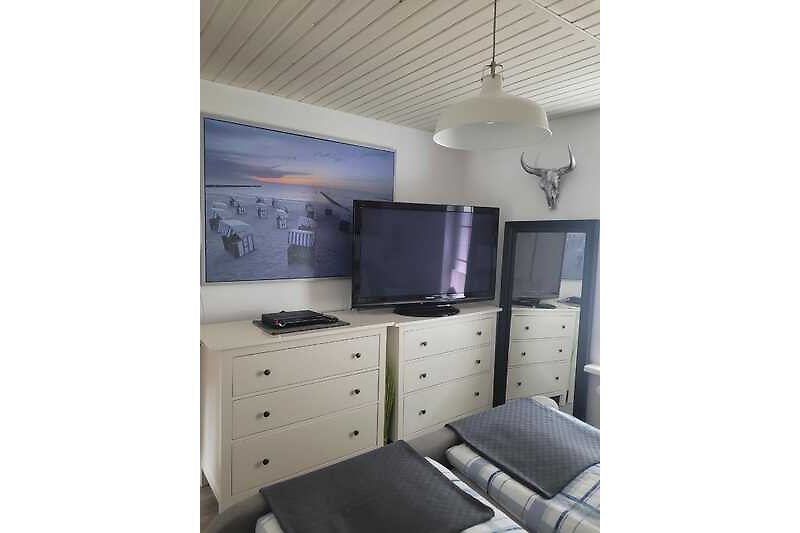 Schlafzimmer mit Bett, Kommode, Lampe und Fernseher.
