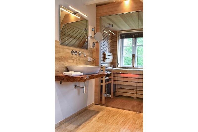 Das grosszügige Badezimmer mit Dusche, freistehender Badewanne und Glasfront-Sauna.